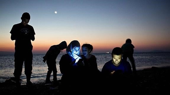 Varios refugiados comprueban sus móviles tras llegar a la isla griega de Kos en agosto.