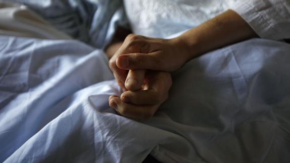 Una mujer sostiene la mano de su madre, enferma de alzheimer. 