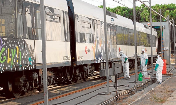 Tres trabajadores con monos y mascarillas limpian las pintadas de un tren de FGV.