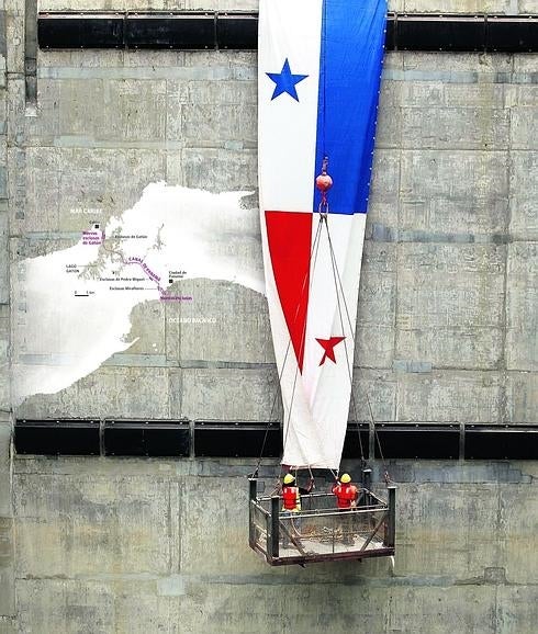 Operarios descuelgan una gran bandera panameña sobre una de las compuertas del nuevo canal para la inauguración.