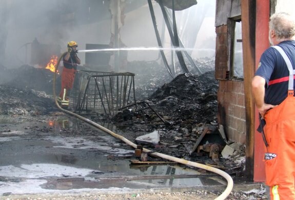 Un bombero sofoca el incendio en el interior de unas las naves arrasadas. :: belén gonzález