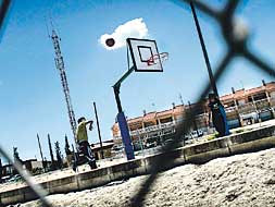 Unos estudiantes juegan en el parque del colegio al baloncesto, a la "sombra" de la antena de telefonía.