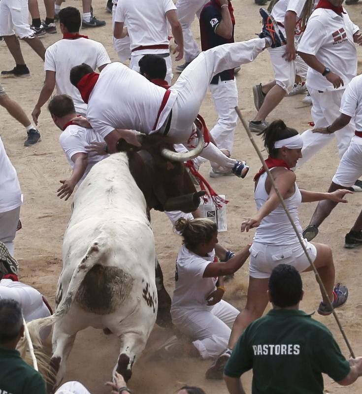 Un toro eleva por el aire con sus astas a un mozo en la plaza.