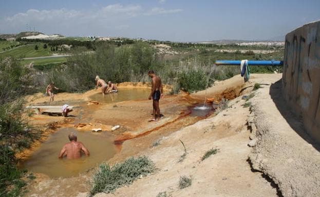 Varias personas se bañan en las pozas termales de la rambla de El Saladillo, alimentadas por un chorro de agua constante.