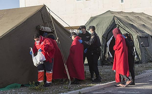 Voluntarios y policías conducen a los rescatados en alta mar hacia las tiendas para prestarles asistencia sanitaria. 