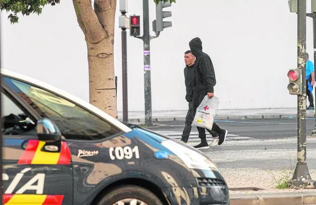 Dos inmigrantes, con una bolsa de la Cruz Roja, el sábado día 4 por la Alameda, cerca de un coche de la Policía Nacional.