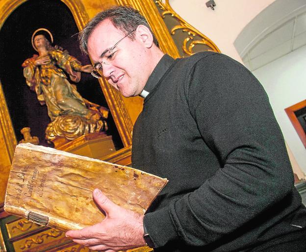 Alegría. El párroco de San Pedro hojea el libro recuperado junto a la talla de Santa Bárbara, de Salzillo.