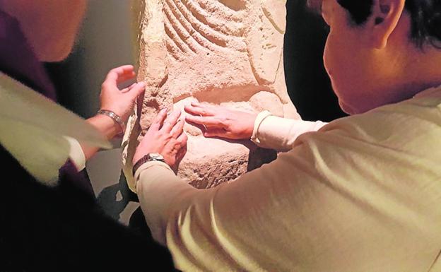 Dos visitantes reconocen el relieve de una obra con sus manos. 