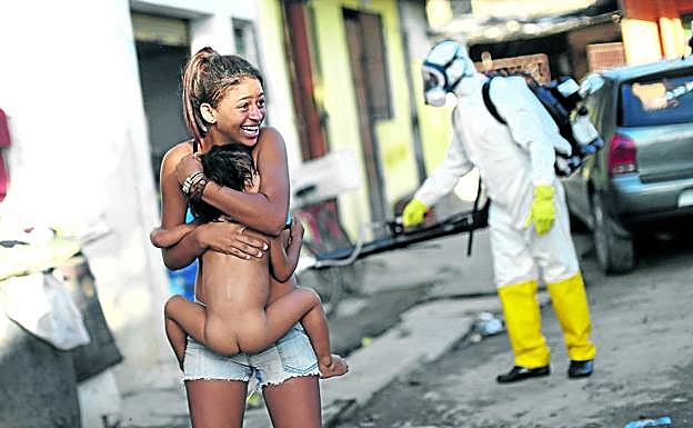 Una mujer brasileña se aleja con su hijo en brazos del operario que rocía insecticida contra el mosquito 'Aedes aegypti' en una calle de Recife. 