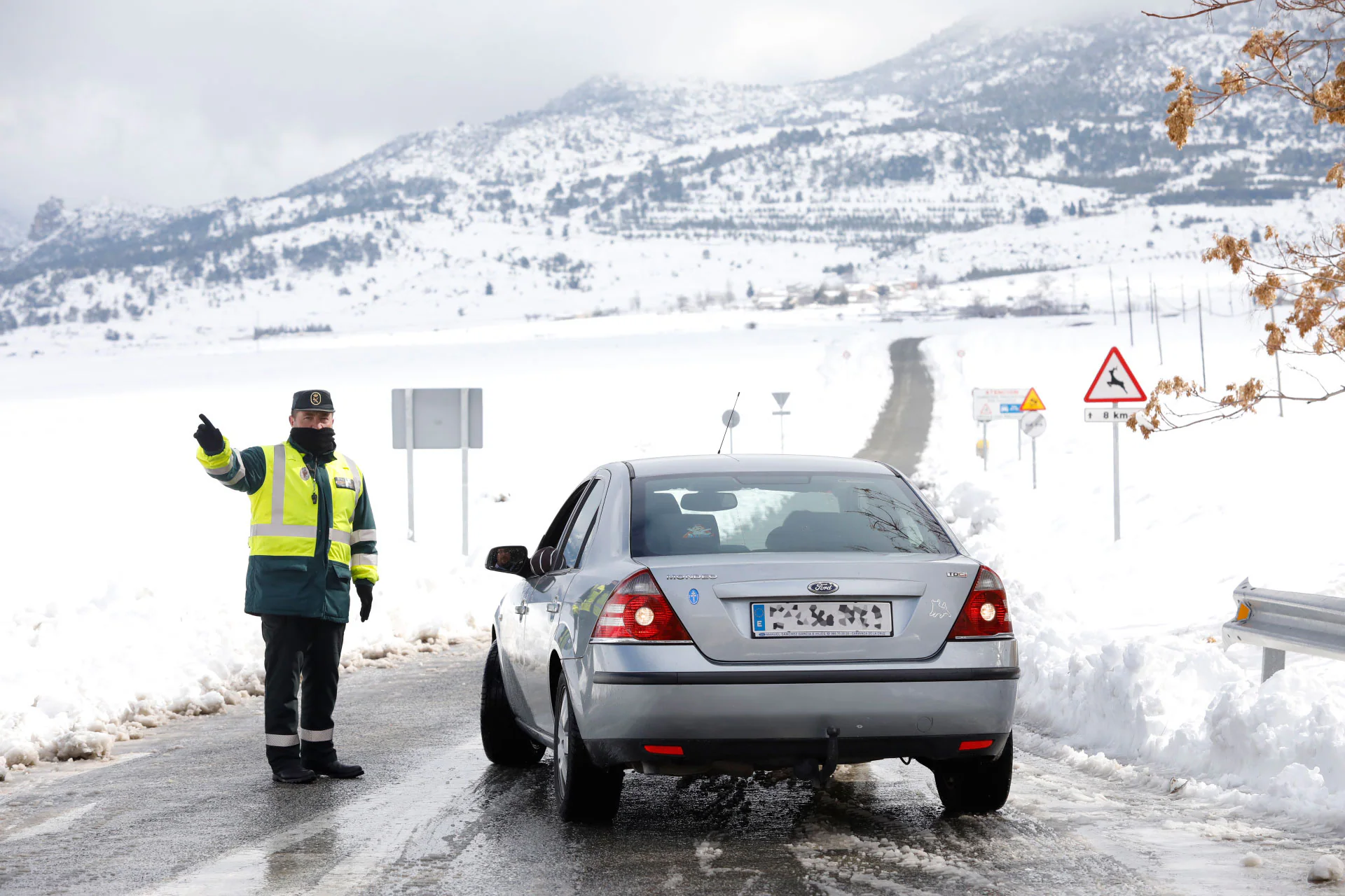 Un guardia civil da indicaciones a un conductor que circula por una carretera nevada.