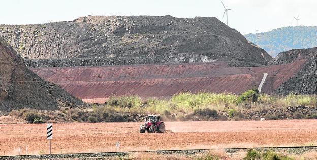 Un agricultor labra con su tractor a los pies de la corta minera Los Blancos I.