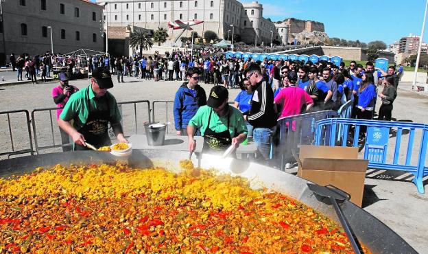 Dos cocineros de la empresas El Tirol reparten platos de paella a los estudiantes, en la explanada del Campus de la Muralla.