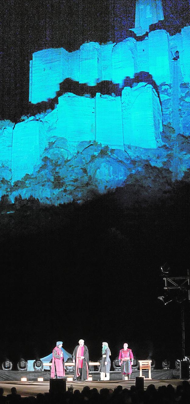 La representación de la obra, con el castillo como fondo iluminado de azul.