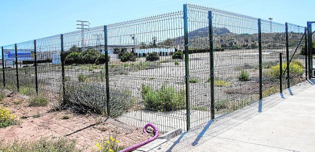 Solar vallado del aparcamiento disuasorio de Cabo de Palos y La Manga y al fondo, la discoteca Trips.