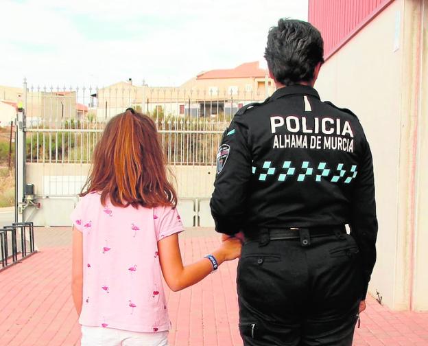 Una niña muestra la pulsera, acompañada de una agente.
