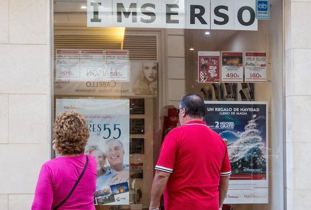 Dos pensionistas miran ofertas en una agencia de viajes con publicidad de los viajes del Imserso