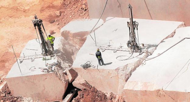 Un enorme bloque de mármol crema marfil es troceado en una cantera.