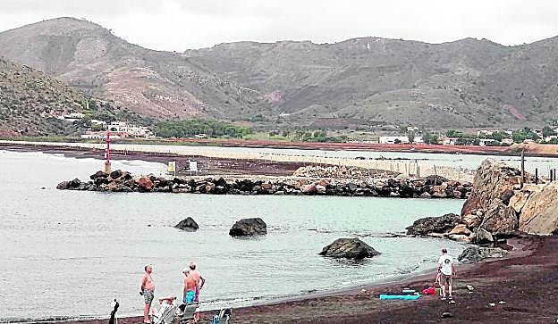 Varios bañistas junto a las obras de dragado de los estériles en la bahía de Portmán. 