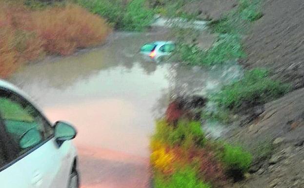 El vehículo hundido, en el centro de la rambla, en Villanueva del Segura, tras anegarse el camino rural por la intensa lluvia. 