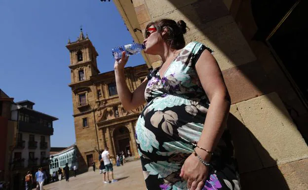 Una mujer embarazada bebe agua en la calle.