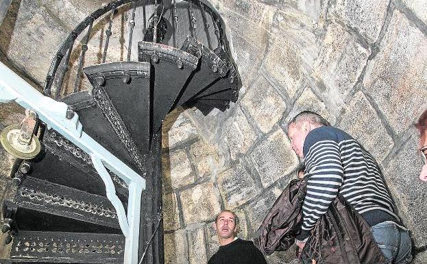 Un guía (i) explica a dos visitantes el tramo final de escalera del faro. 