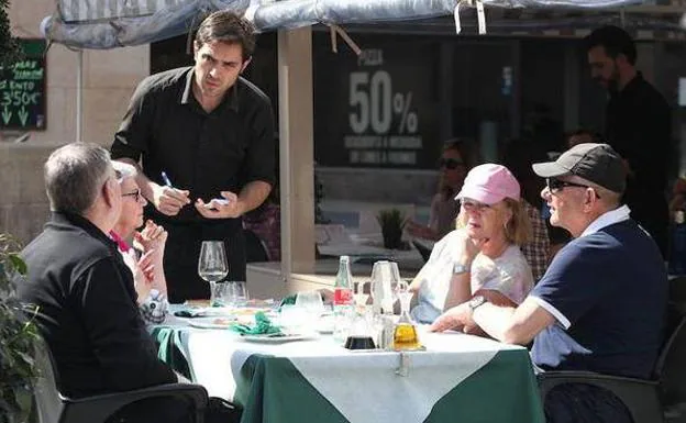 Un camarero sirve a unos clientes en la terraza de un bar.