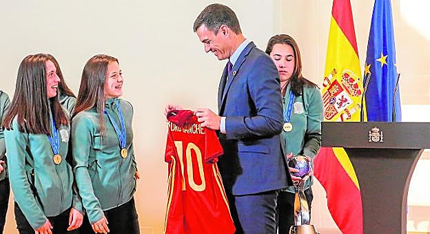 El presidente del Gobierno, Pedro Sánchez, recibe la camiseta de la selección con su nombre de parte de la yeclana Eva Navarro, a la izquierda, Claudia Pina y Cata Coll. 