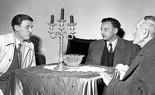 Castillo-Puche, a la izquierda, con el bliotecario, bibliógrafo y crítico Justo García Morales y Azorín, sentados en una mesa de camilla. 