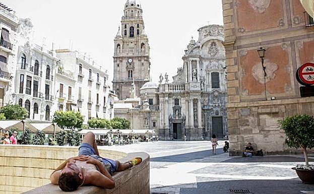 Un joven combate el calor a la sombra frente a la catedral en una foto de archivo.