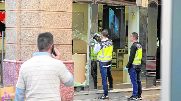 Dos investigadores de la Policía Nacional hacen fotos del boquete realizado por los ladrones en la tienda. 