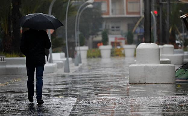 Un peatón camina bajo la lluvia en Murcia.