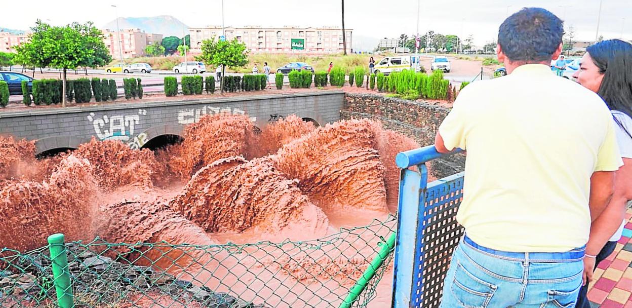 Dos vecinos observan la virulencia del agua al chocar contra los pilares de la rambla, en la rotonda de la 1900, junto a Nueva Cartagena. 