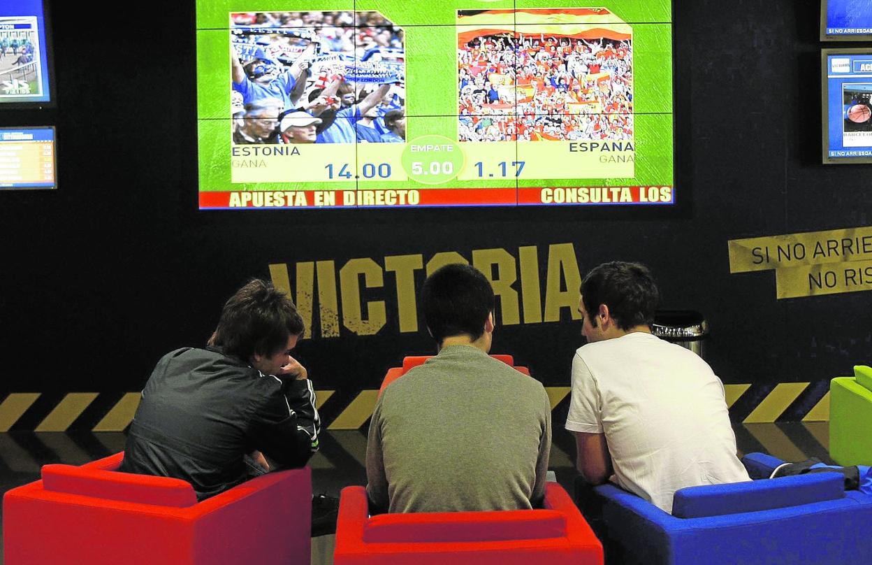 Tres jóvenes comparten impresiones en un salón de apuestas deportivas. 