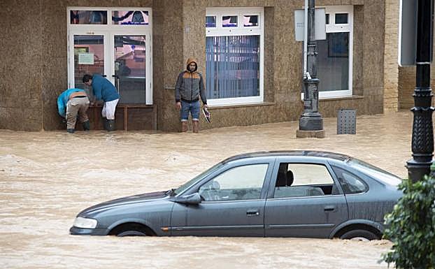 Vecinos de Los Alcázares tratan de evitar que entre agua en un comercio este martes. 