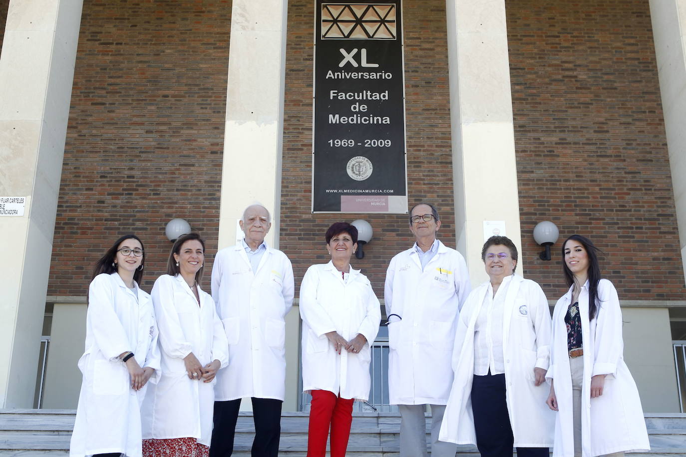 09-06-2019. Una Facultad de oro. La Comunidad entrega uno de sus cinco máximos galardones a la Facultad de Medicina, que lleva 50 años formando a excelentes profesionales para beneficio de todos. Nacida de manera precaria, sin instalaciones propias ni un hospital clínico, la Facultad de Medicina de la UMU es la cuarta más cotizada de España, con 3.000 solicitudes para 200 plazas. En la foto, estudiantes, directivos, profesores eméritos y exalumnos con las mejores notas en el exigente MIR, en la entrada de la Facultad. :: Martínez Bueso
