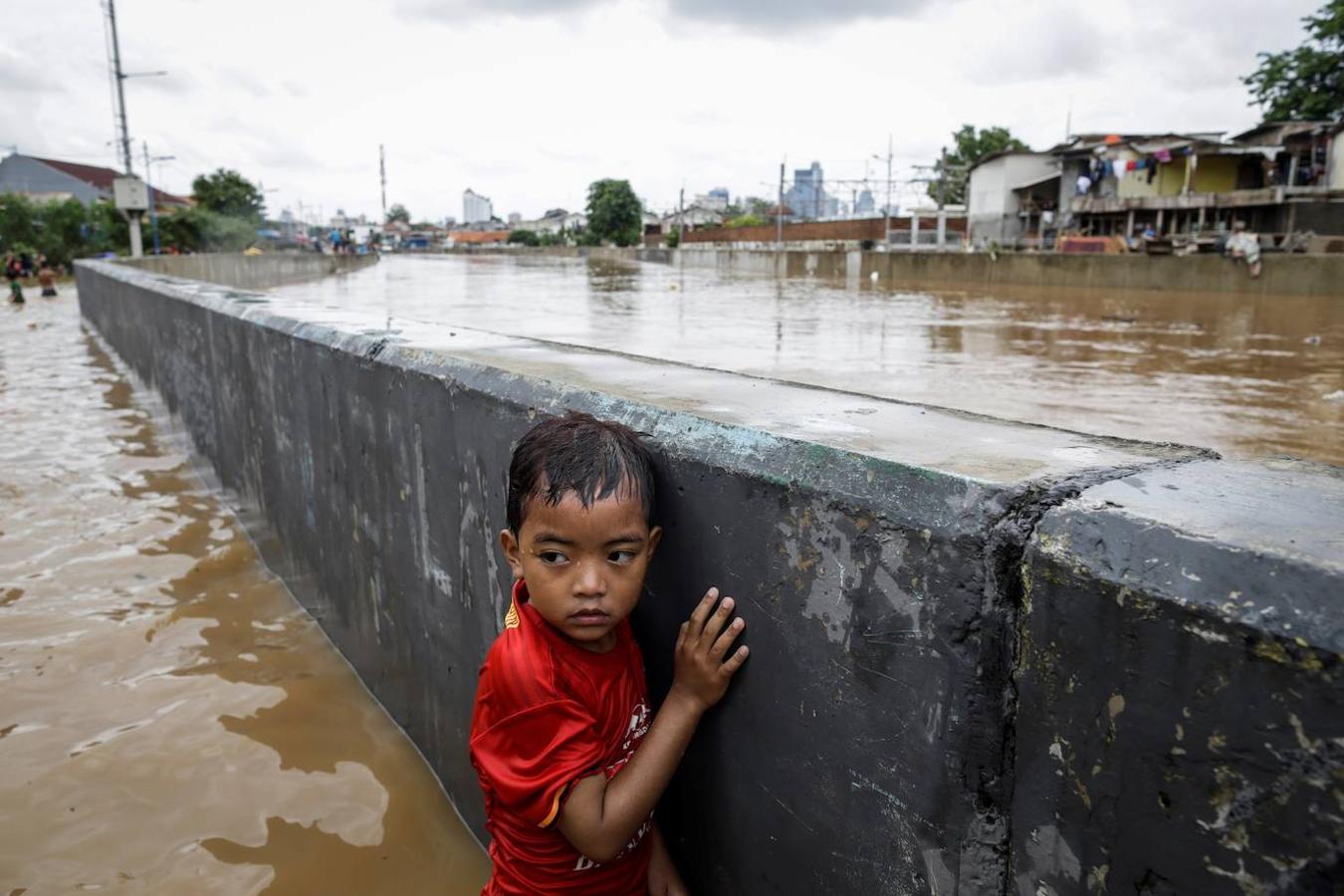 Un niño empapado se sujeta a un muro en medio de las inundaciones de Yakarta, Indonesia.