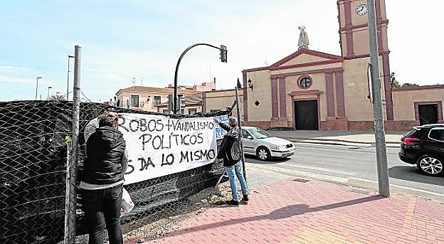 Dos vecinos de La Palma colocan una pancarta en la valla de un solar ubicado frente a la iglesia. 