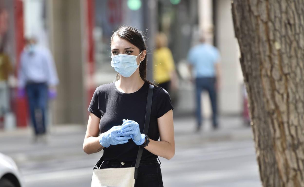 Una chica camina con mascarilla y guantes duante el estado de alarma. 