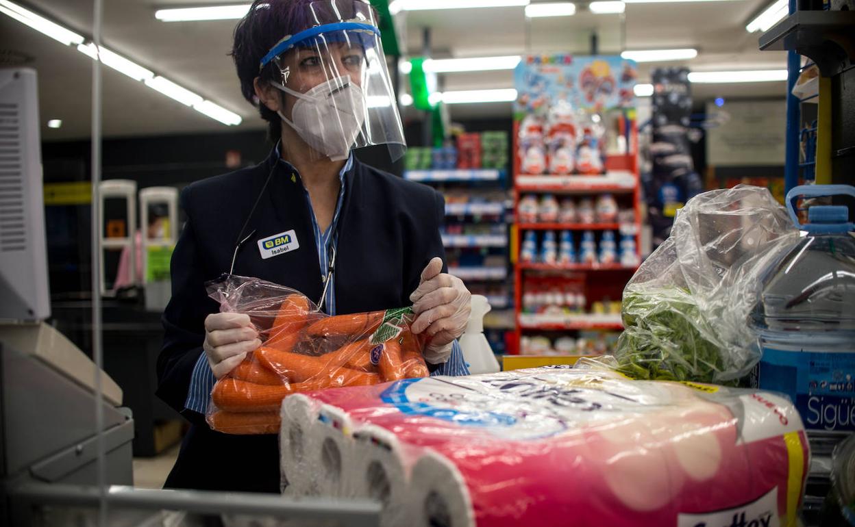 Una cajera de un supermercado, con guantes, mascarilla y visera de proteccion