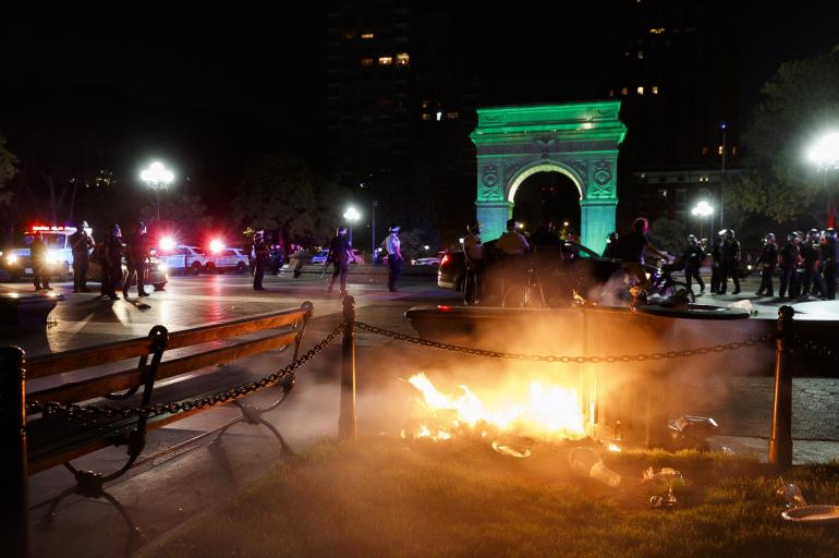 En la imagen se puede ver a los policías de la ciudad en el fondo y de frente, un incendio provocado por manifestantes en el icónico parque de Washington Square