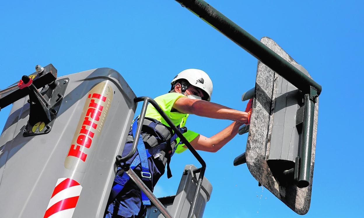 Un trabajador, subido a la cesta de un camión grúa, limpia la unidad óptica de un semáforo. 