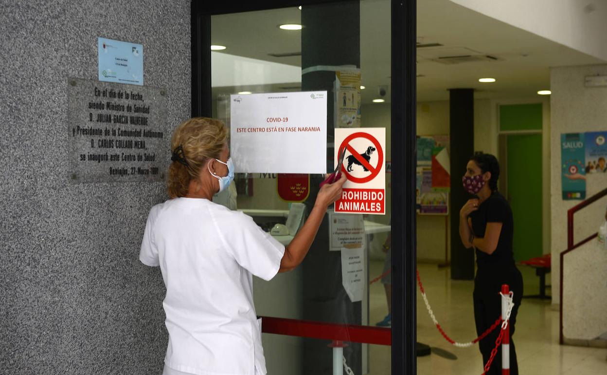 Una sanitaria pega un cartel alertando de la 'fase naranja', este viernes, en el centro de salud de Beniaján.