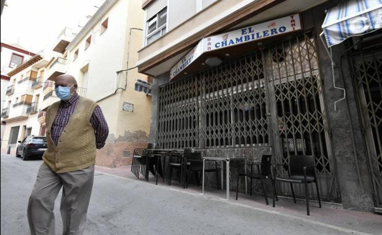 Un vecino de Abanilla, protegido por una mascarilla, caminando frente a uno de los bares de la localidad, con sus puertas cerradas.