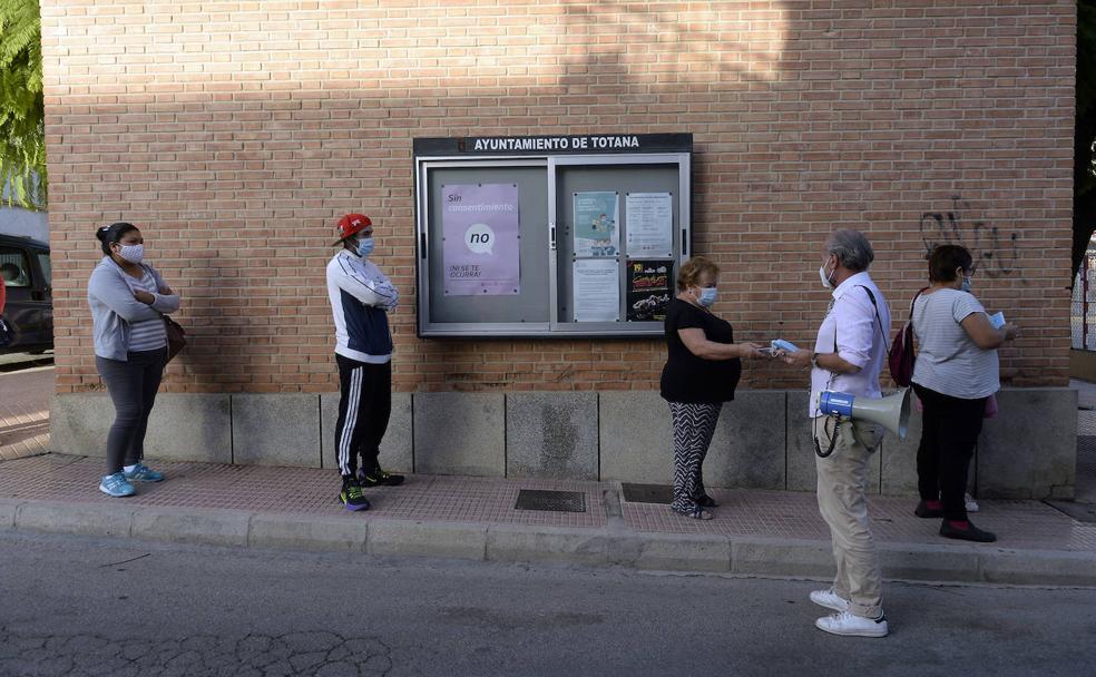 El médico Abel Novoa reparte mascarillas a vecinos del barrio de la Era Alta de Totana, que hacen cola para realizarse el test de antígenos, el pasado martes.