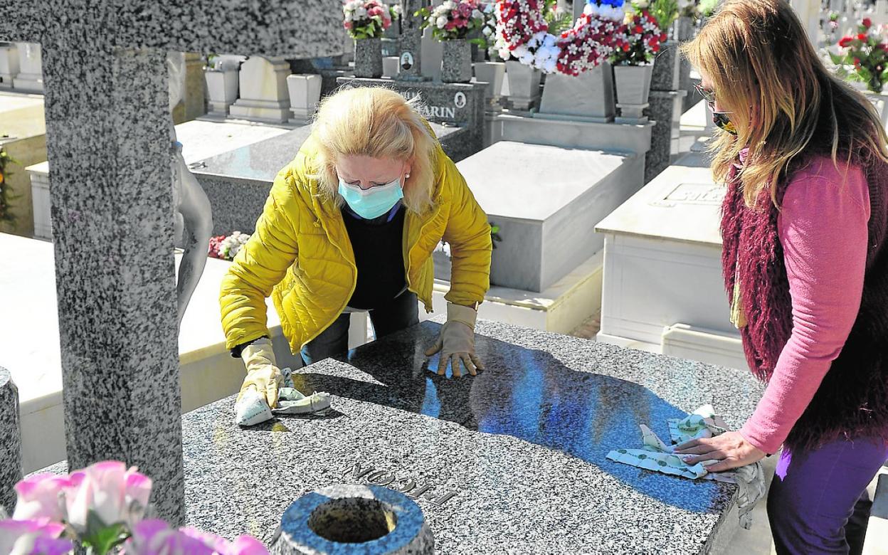 Dos mujeres, este martes en el cementerio, limpian la tumba familiar. 