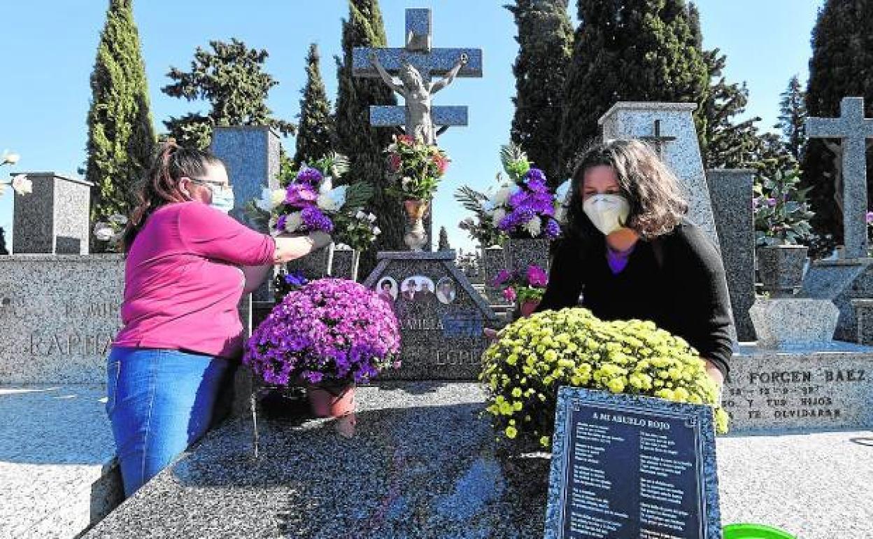 Mujeres con mascarilla colocan flores en el cementerio de Murcia.