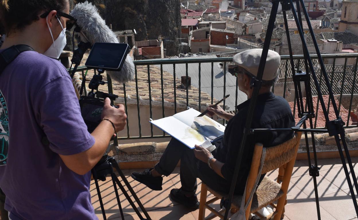 Rodaje del documental con Pedro Cano en una silla de enea pintando Blanca en un cuaderno. 