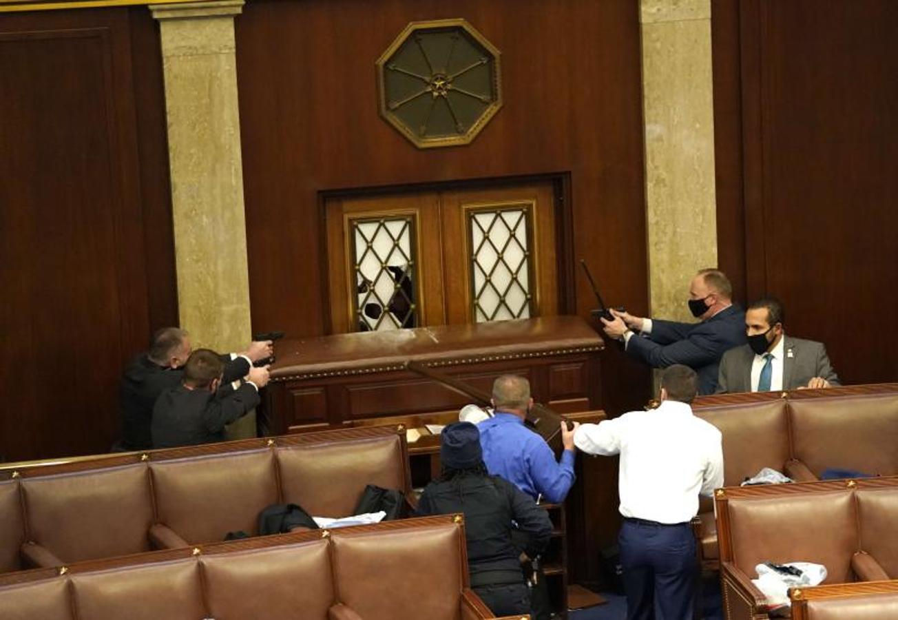 Los agentes del orden apuntan con sus armas a una puerta que fue asaltada en la Cámara de Representantes durante una sesión conjunta del Congreso