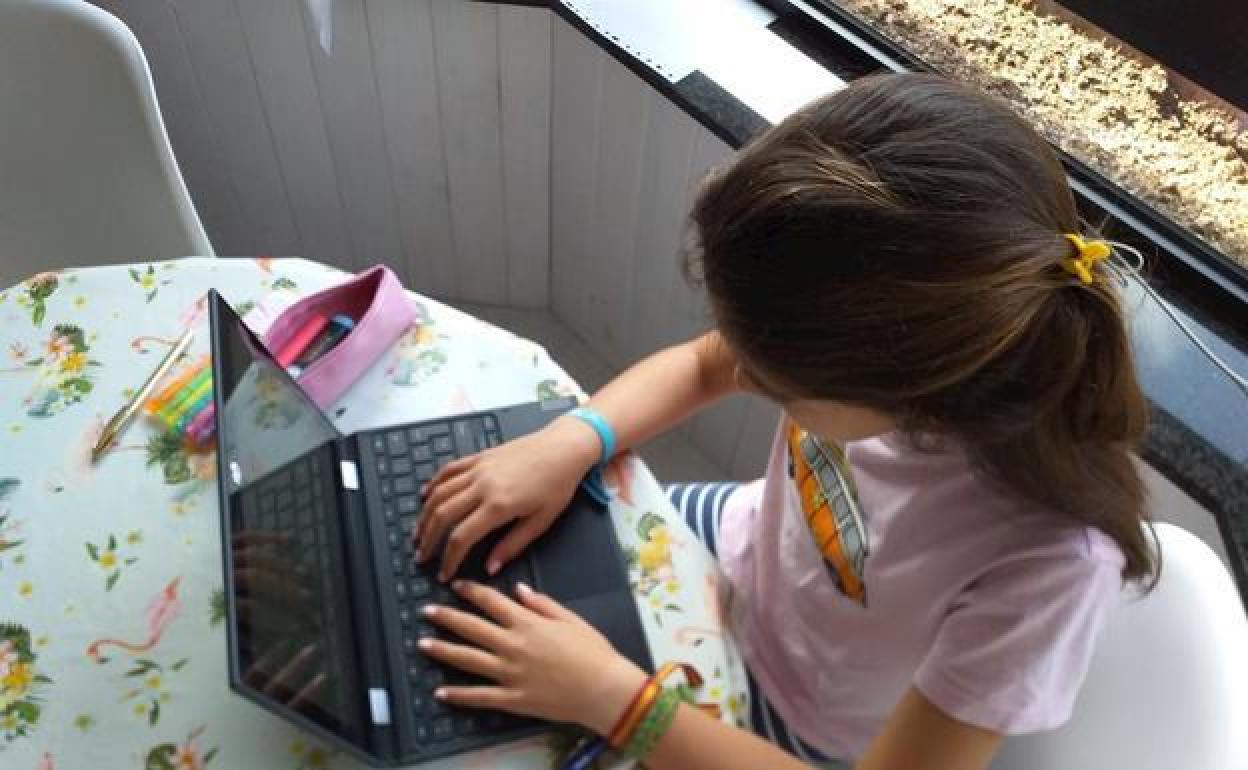 Una niña haciendo los deberes con un ordenador portátil en una foto de archivo.