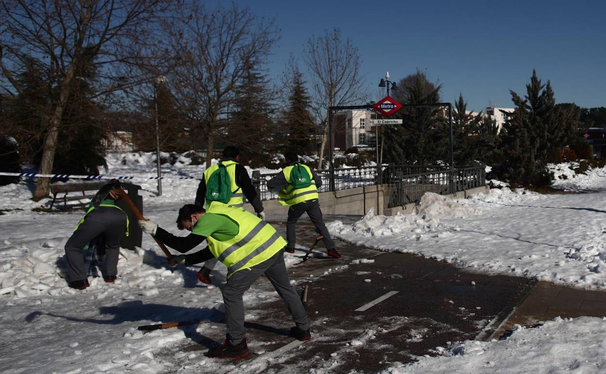 Un grupo de personas trabaja despejando nieve en el acceso al metro El Capricho en el distrito de Ciudad Lineal en Madrid.